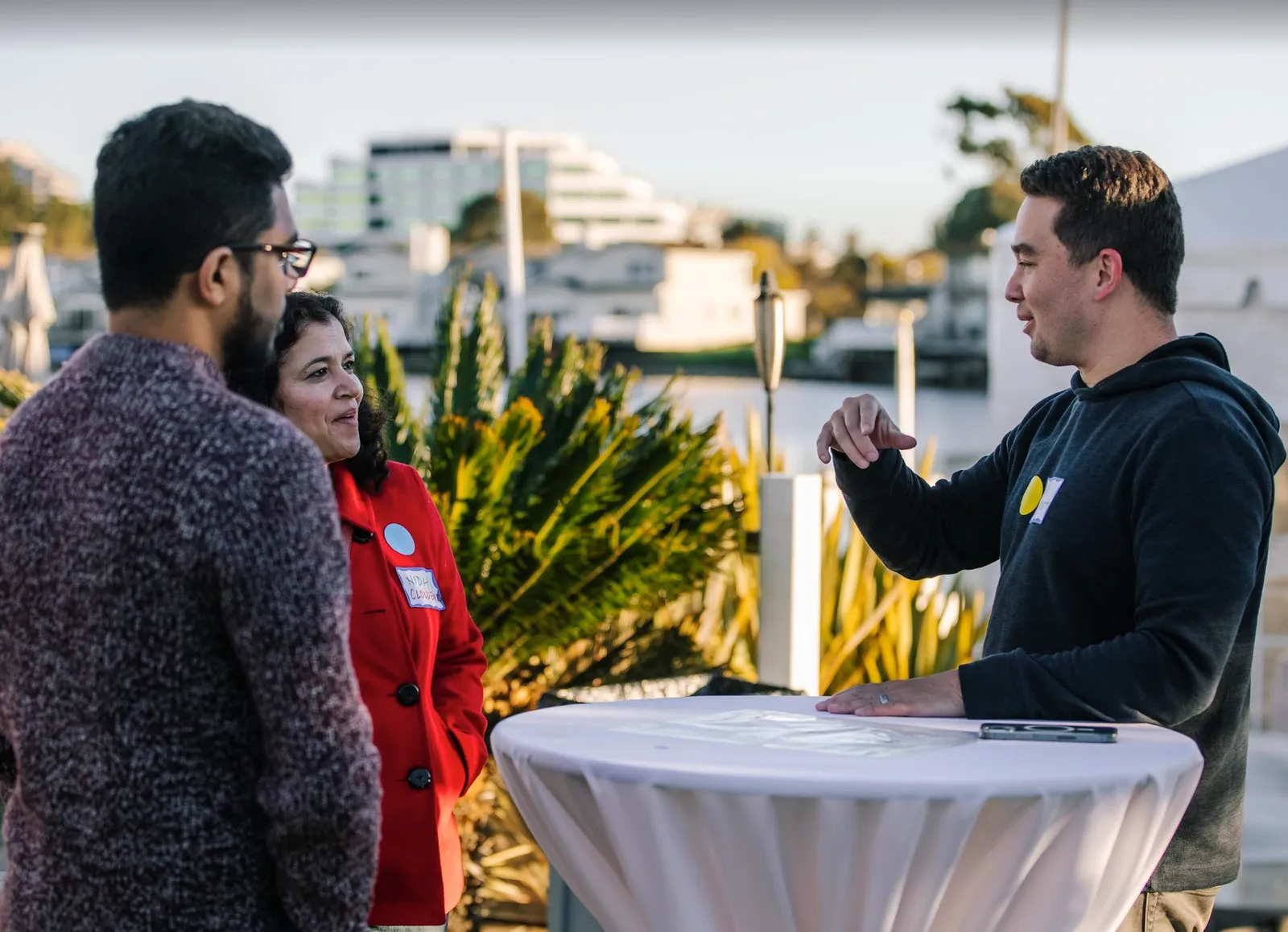 A small, intimate conversation among a few founders standing around a cocktail table outdoors.